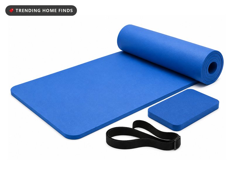 A thick blue exercise mat partly rolled with a matching knee pad and a black carrying strap.