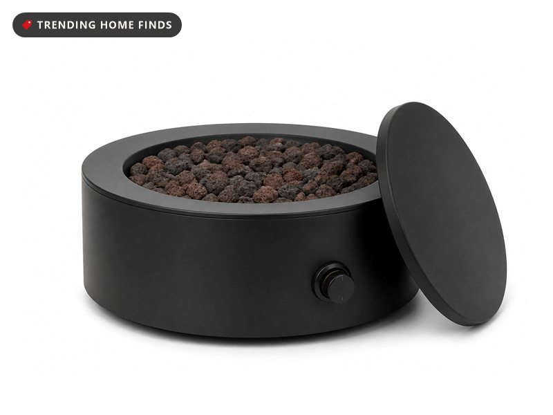 A round black propane fire pit with lava rocks in the middle and a flat lid leaning on its side.