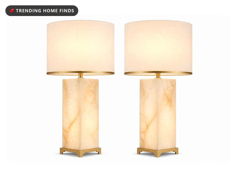 Two matching alabaster column lamps with white linen shades trimmed in gold, switched on.