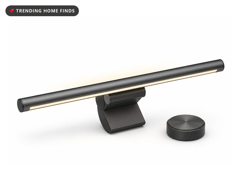 A slim dark gray monitor light bar on a clamp, lit warm from below and glowing from its back, with a round puck controller.