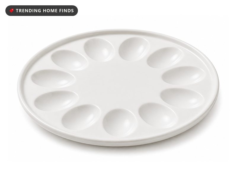 A round white porcelain deviled egg platter with twelve oval wells set around the surface.