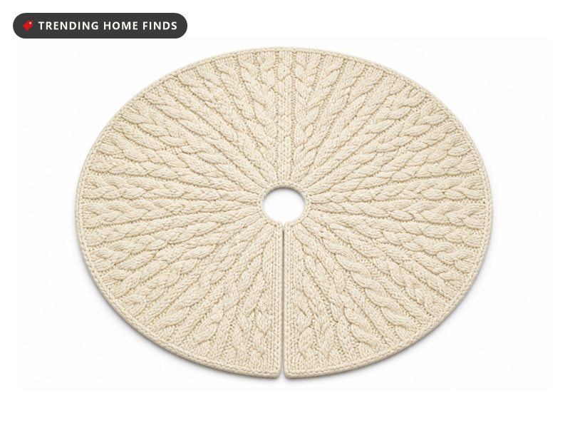 A round cream cable knit Christmas tree skirt laid flat with a small opening at its center.