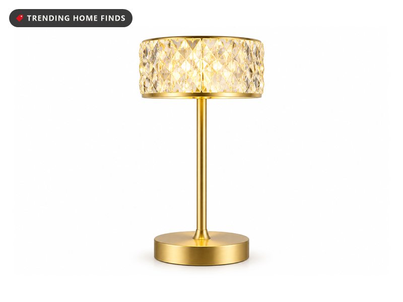 A cordless lamp with a gold metal base and a clear faceted crystal shade glowing warm.