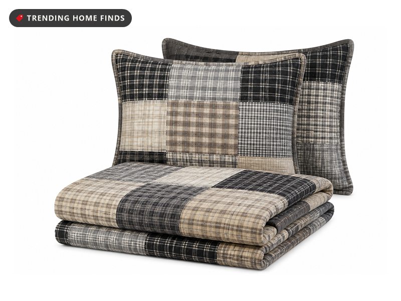 A folded patchwork quilt in a gray, tan and black plaid with two matching pillow shams.