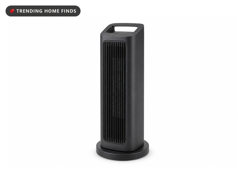 A slim dark gray tower space heater with a vertical front grille and a recessed carry handle, seen from a low angle.