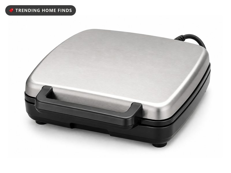 A compact electric pizzelle press with a brushed silver top shell, a black base and a front handle.