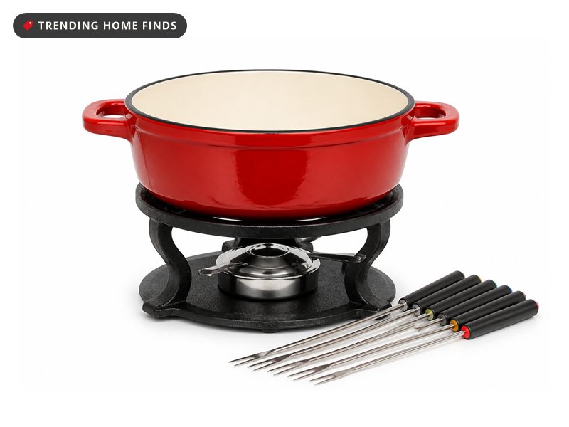 A glossy red enameled cast iron fondue pot on a black stand with six long fondue forks beside it.