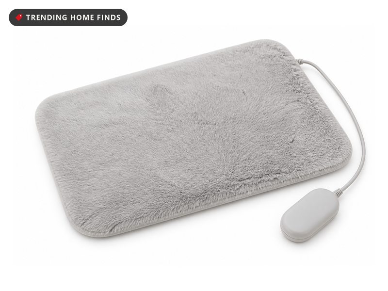 A light gray faux fur electric foot warmer pad with a thin cord and a small controller.