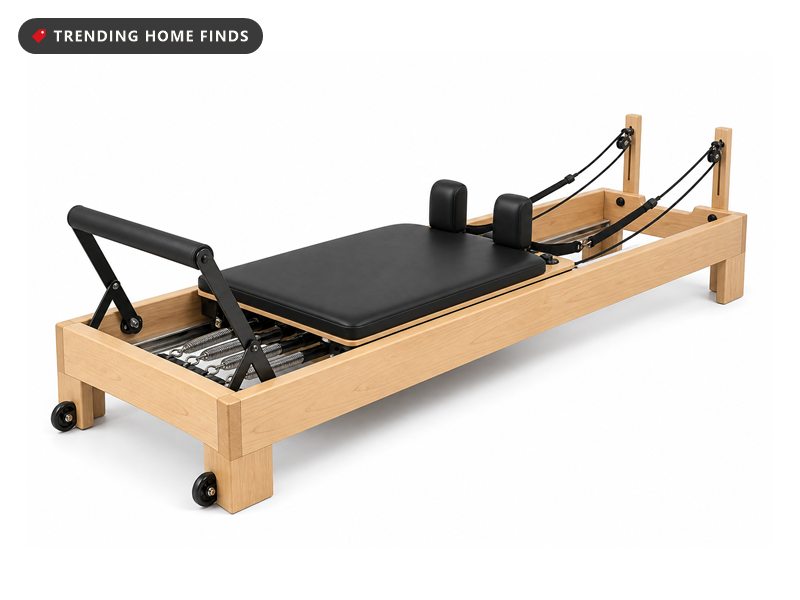 A light wood pilates reformer with a padded sliding carriage, springs, shoulder rests and a foot bar.