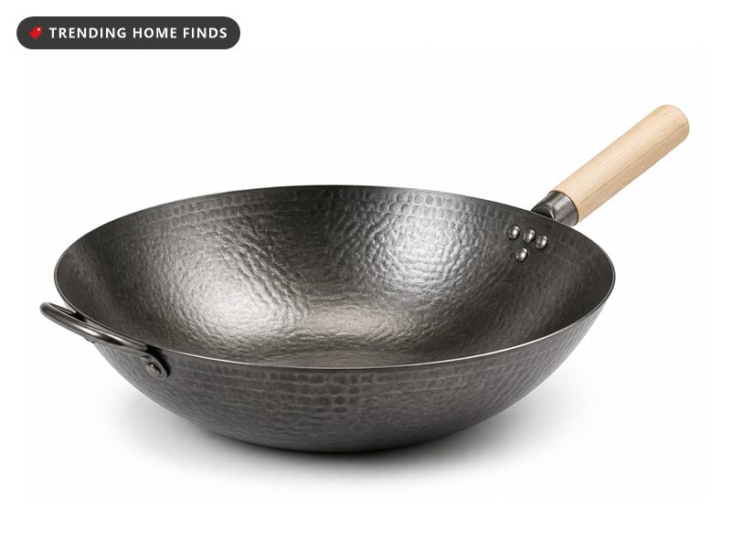A hand hammered carbon steel wok with a pale wooden handle and a small steel helper handle on the far rim.