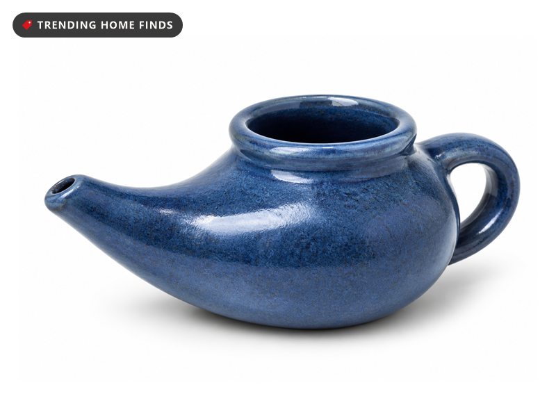 A small handcrafted blue glazed ceramic neti pot with a tapered spout and a rounded handle.