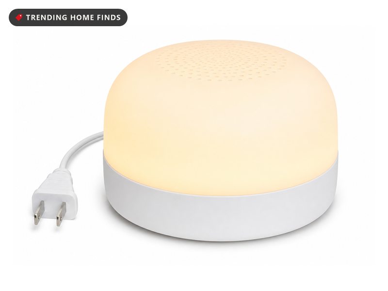 A round white sound machine with a built in glow light, a small dome on a flat base glowing soft amber.