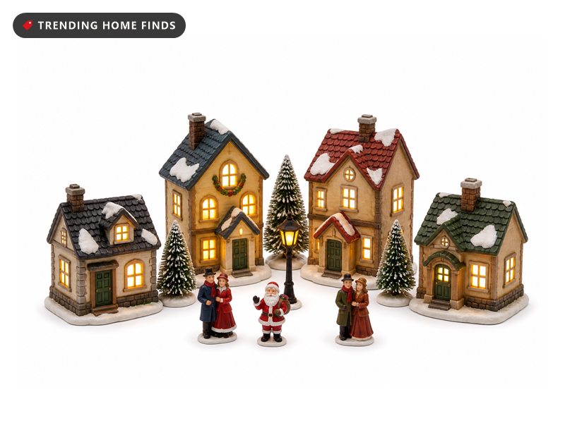 A lighted Christmas village with four glowing houses, trees, a street lamp and small figurines.