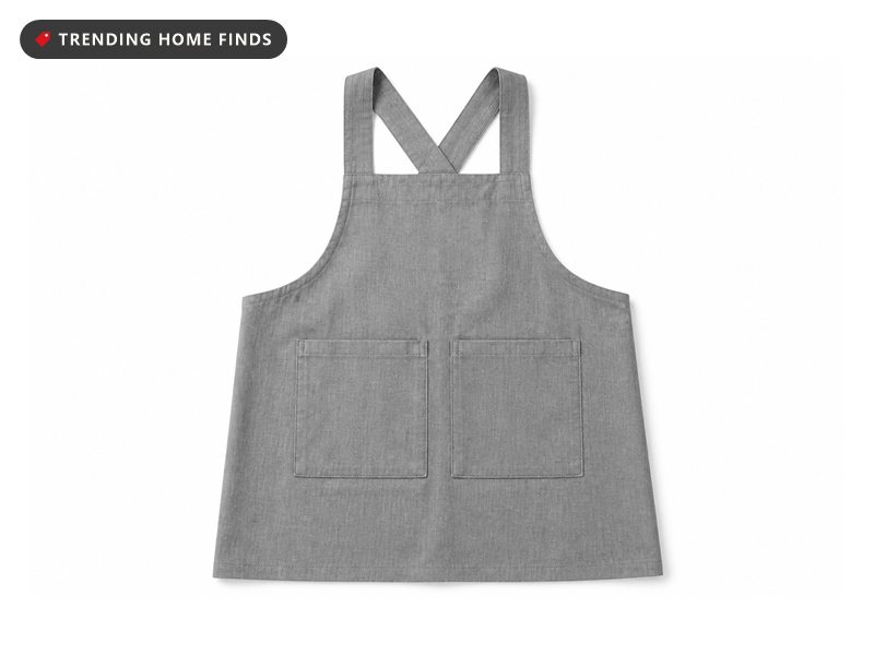 A gray cotton linen apron with crossed back straps and two front pockets laid flat.