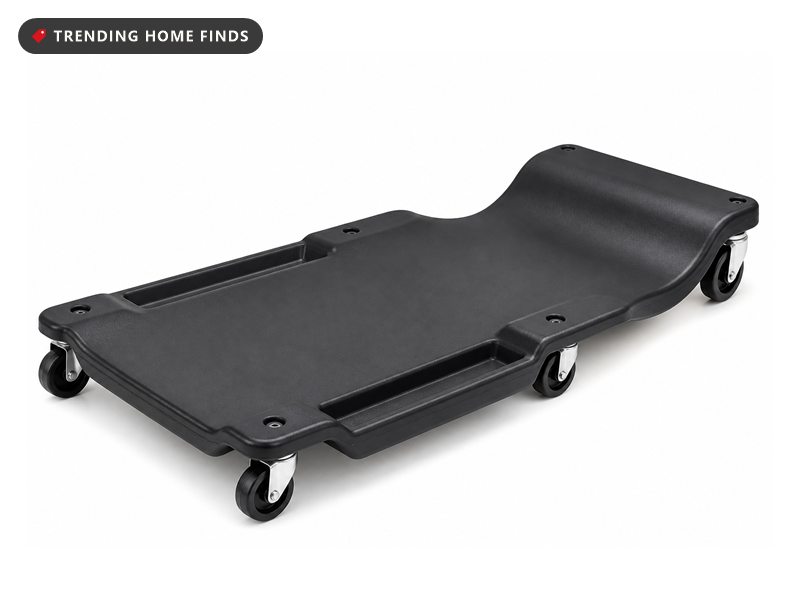 A long low profile black plastic mechanic creeper with a raised head end, molded tool trays and rolling casters.