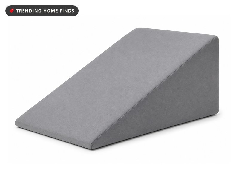 A gray fabric covered foam wedge pillow with its thick end upright and a long sloping top.