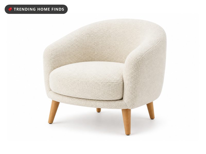 A cream boucle barrel armchair with a curved wrap around back and four tapered wood legs.