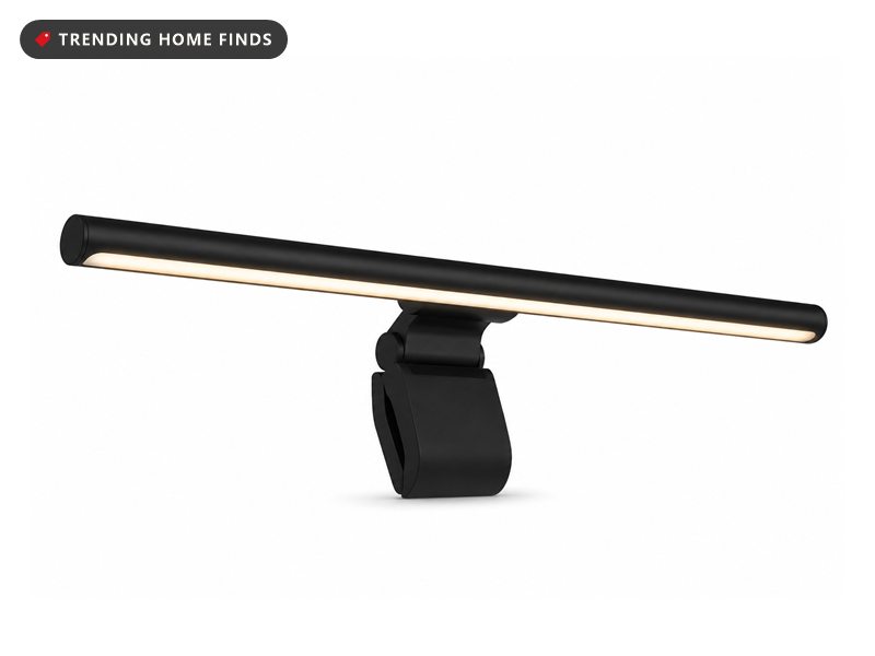 A slim black monitor light bar glowing warm along its underside on a counterweight clip.