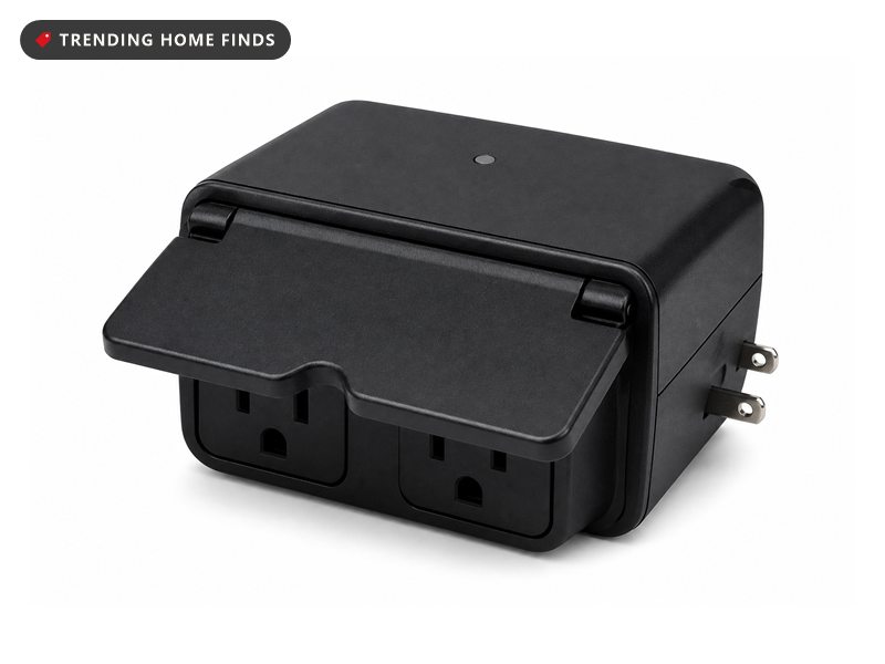 A black weatherproof outdoor smart plug with a hinged cover over two downward facing sockets.