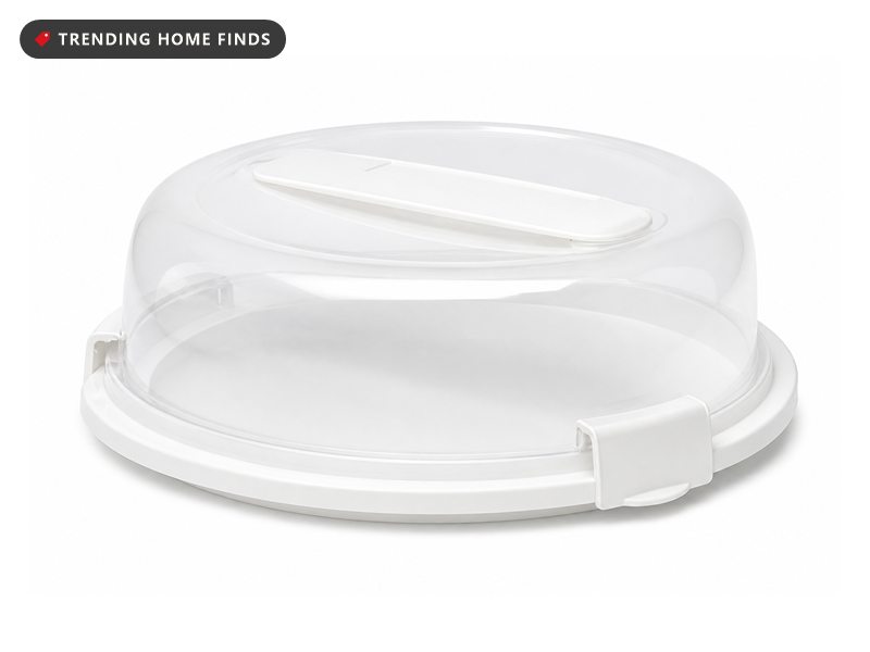 A white round plastic pie carrier with a clear domed lid clamped onto the base and a flat folding handle.