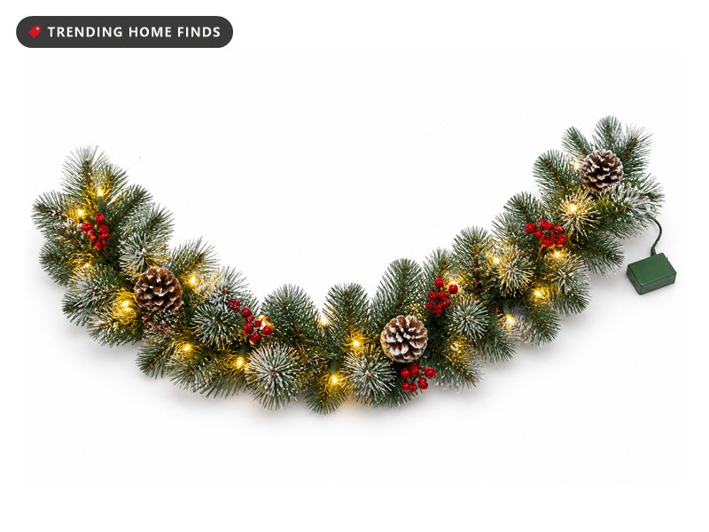 A prelit pine garland with red berries, pinecones and glowing warm white lights laid in a curve.