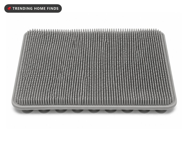 A gray silicone foot scrubber mat covered in dense soft bristles with suction cups.
