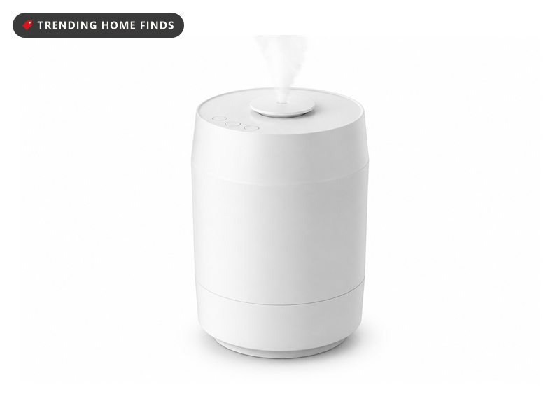 A tall white cylindrical humidifier with a round nozzle on the lid releasing a fine mist.