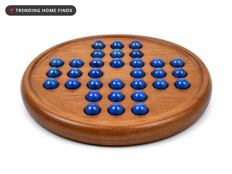 A round solid wood marble solitaire board with blue glass marbles seated in shallow drilled recesses.