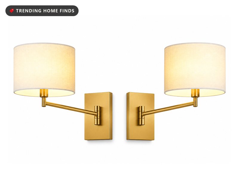 Two warm gold swing arm wall lamps with white linen drum shades, arms angled outward.