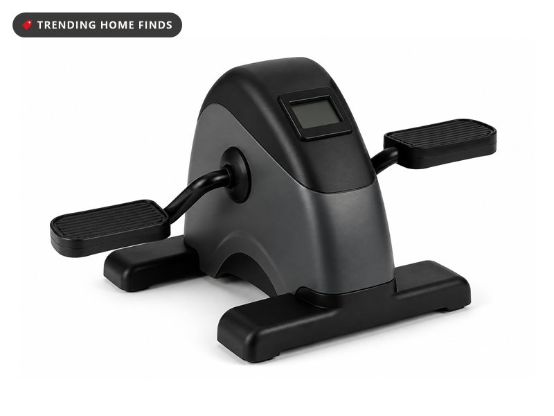 A compact black and gray pedal exerciser with two flat pedals and a small blank display.