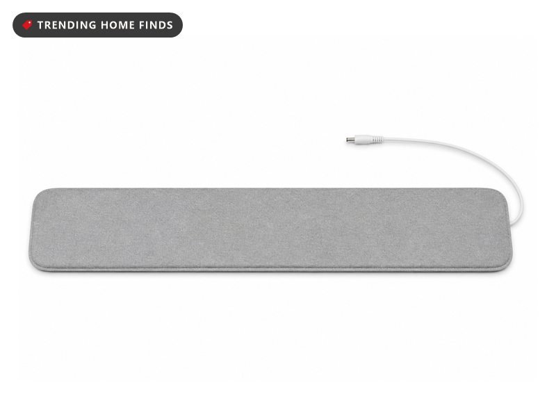 A thin gray fabric sleep tracking pad with rounded corners and a thin white cable and plug.
