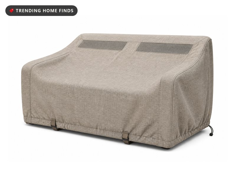 A beige and gray outdoor furniture cover fitted over a loveseat form with a drawstring hem and buckle straps.