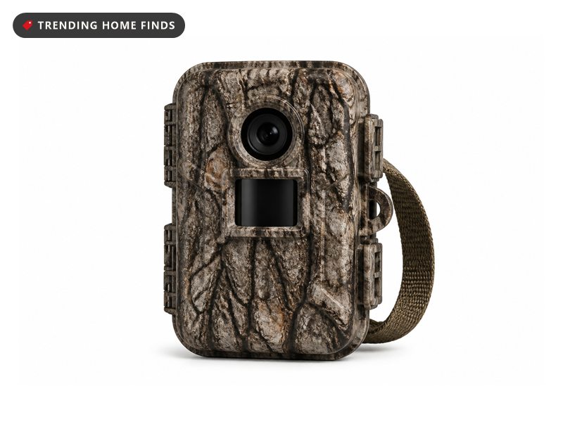 A compact camouflage trail camera with a round dark lens and a small sensor panel and a mounting strap.