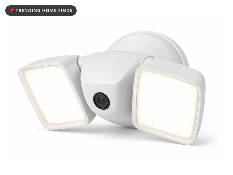 A white floodlight security camera with two angled light panels switched on and a small round lens between them.