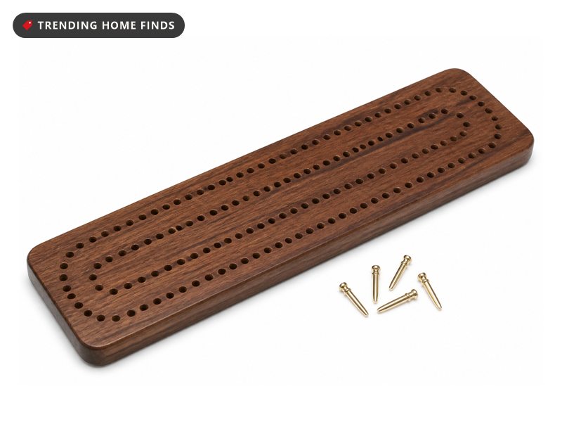 A long walnut stained cribbage board with three tracks of peg holes and a few metal pegs beside it.
